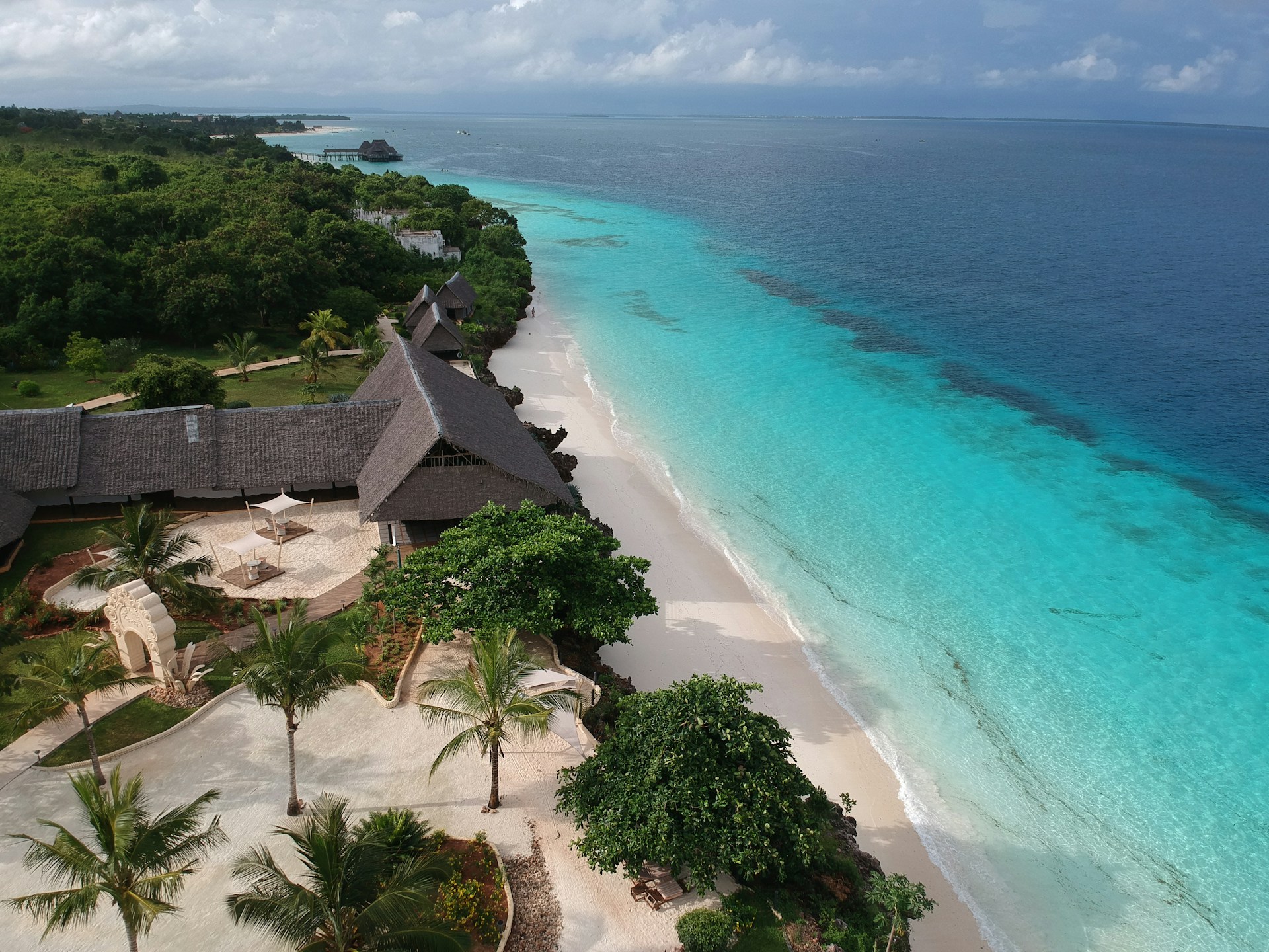 Aerial view of a thatched-roof beach resort on white sand next to turquoise ocean in Zanzibar